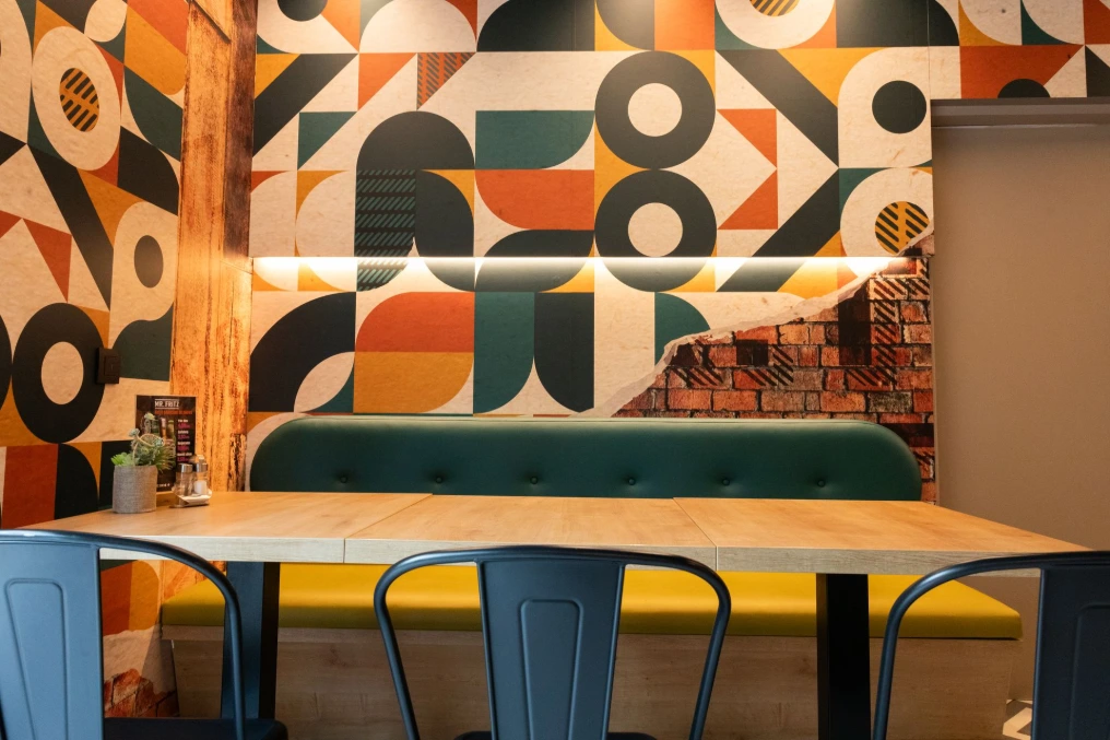 Banquette verte sous la fresque géométrique, tables en bois et chaises noires — Mr Fritz Fontaine