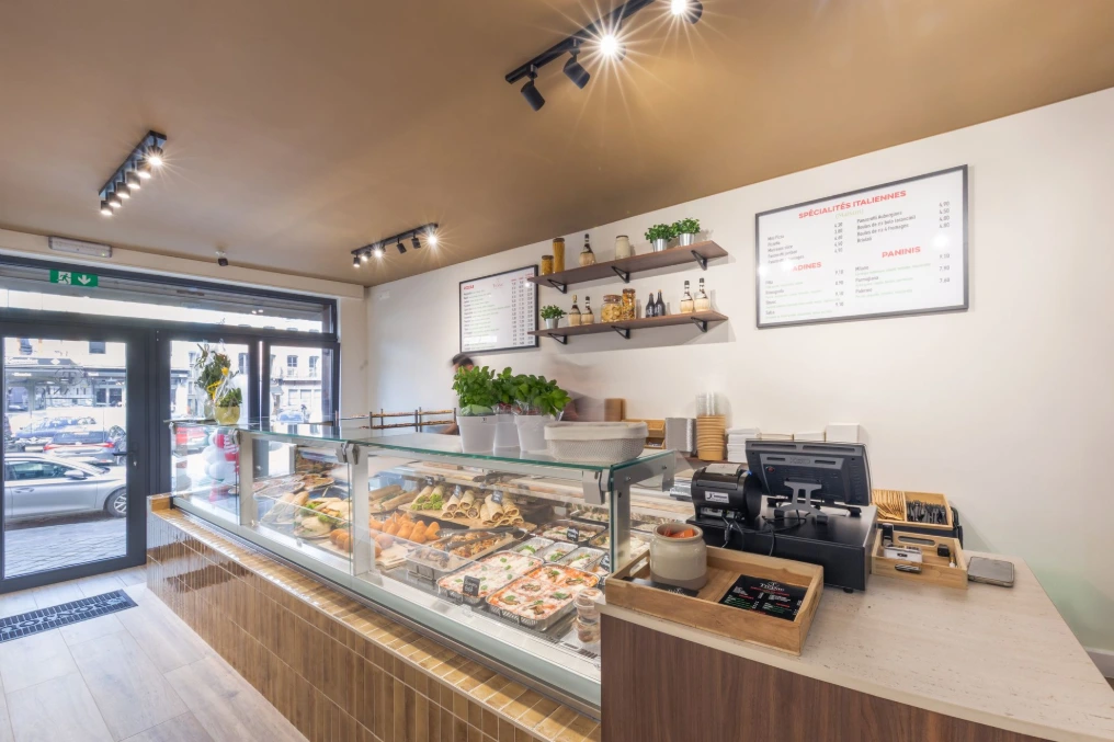 Vue depuis l'entrée : vitrine traiteur, caisse et éclairage sur rail — Pizzeria Traiteur Titanic
