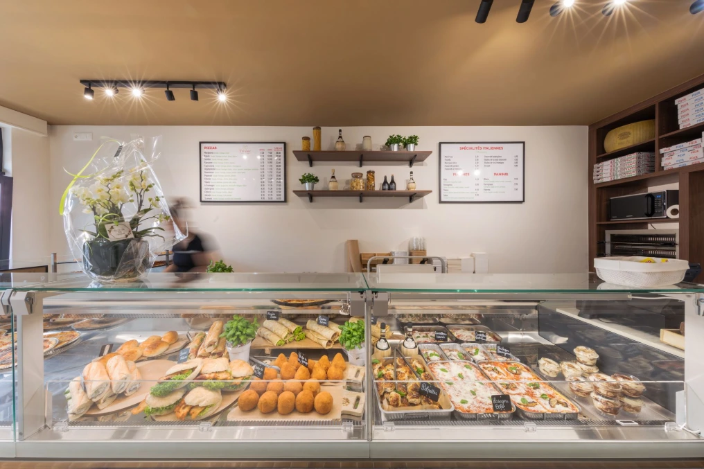 Comptoir de vente et vitrine réfrigérée sous les étagères murales — Pizzeria Traiteur Titanic