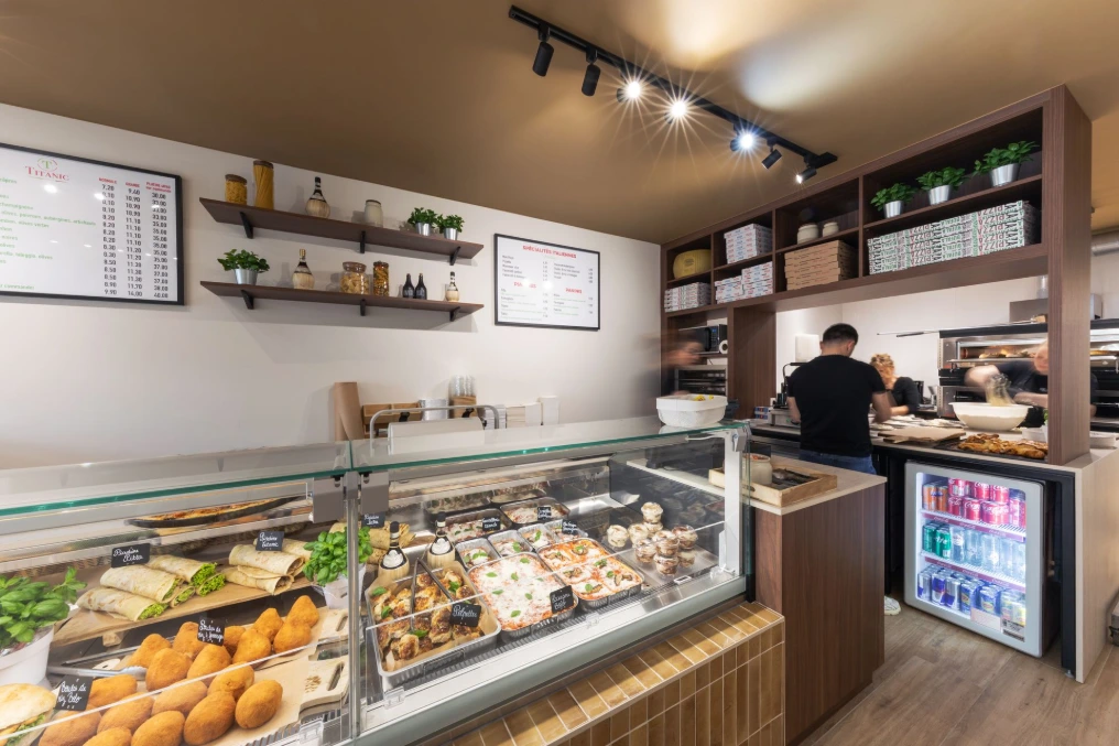 Comptoir traiteur avec vitrine réfrigérée, étagères murales et cadres décoratifs — Pizzeria Traiteur Titanic