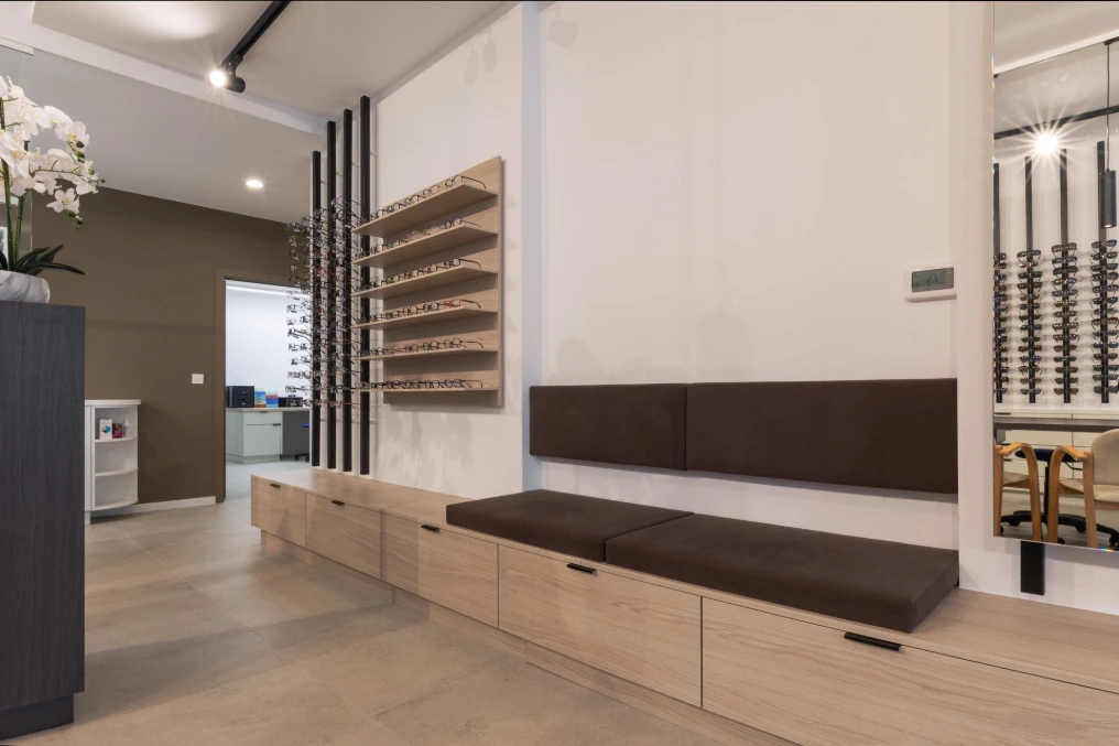 Banquette d'attente en cuir brun sous les présentoirs à lunettes — Optique Lecapitaine