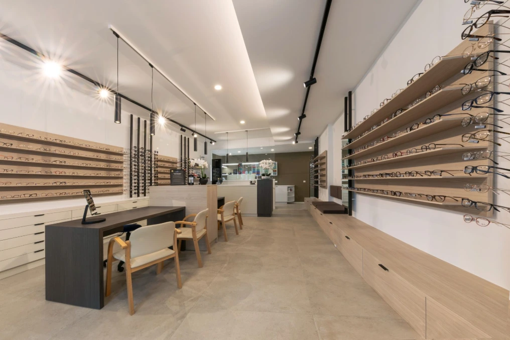 Présentoirs muraux en bois, table d'essayage et sol clair — Optique Lecapitaine