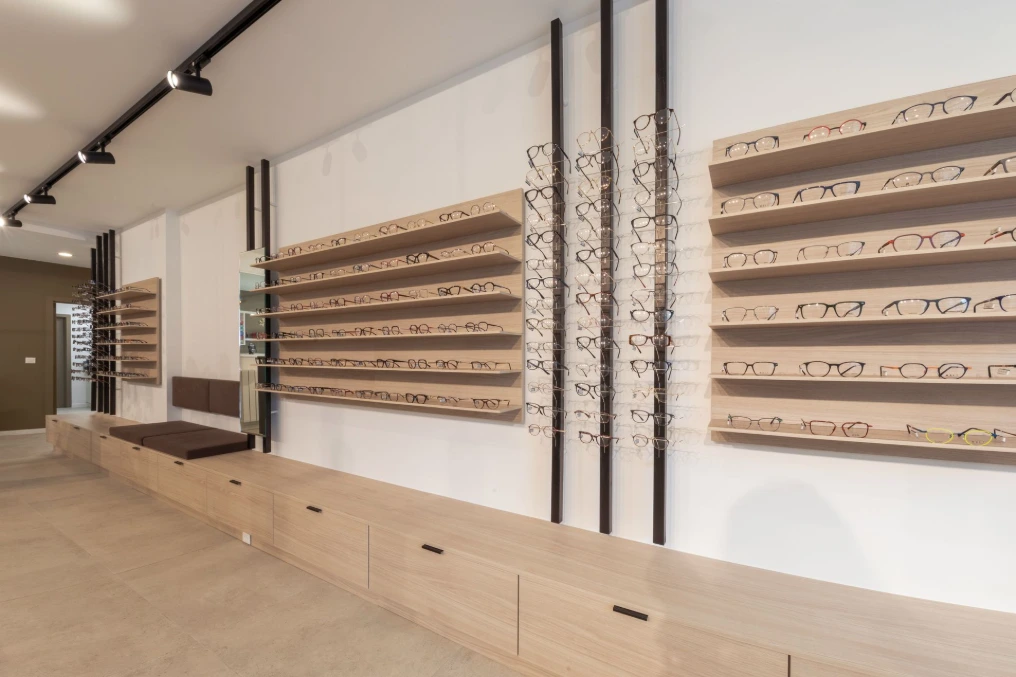 Mur de présentation des montures sur tablettes en bois et meuble bas à tiroirs — Optique Lecapitaine