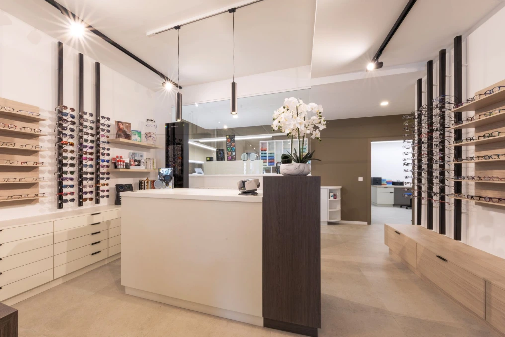 Comptoir de vente clair au centre du magasin, entouré de présentoirs — Optique Lecapitaine