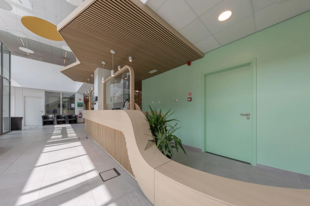 Banque d'accueil courbe en bois clair devant la paroi vitrée verte — Service Public de Wallonie