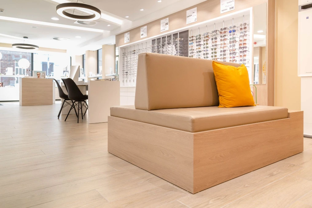 Banquette d'attente en bois clair avec coussin orange — Optique Bernard