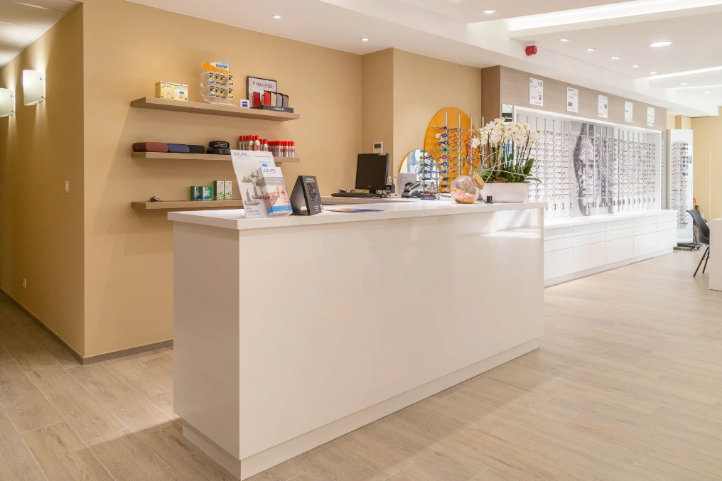 Comptoir d'accueil blanc et rayonnages muraux dans les tons chauds — Optique Bernard