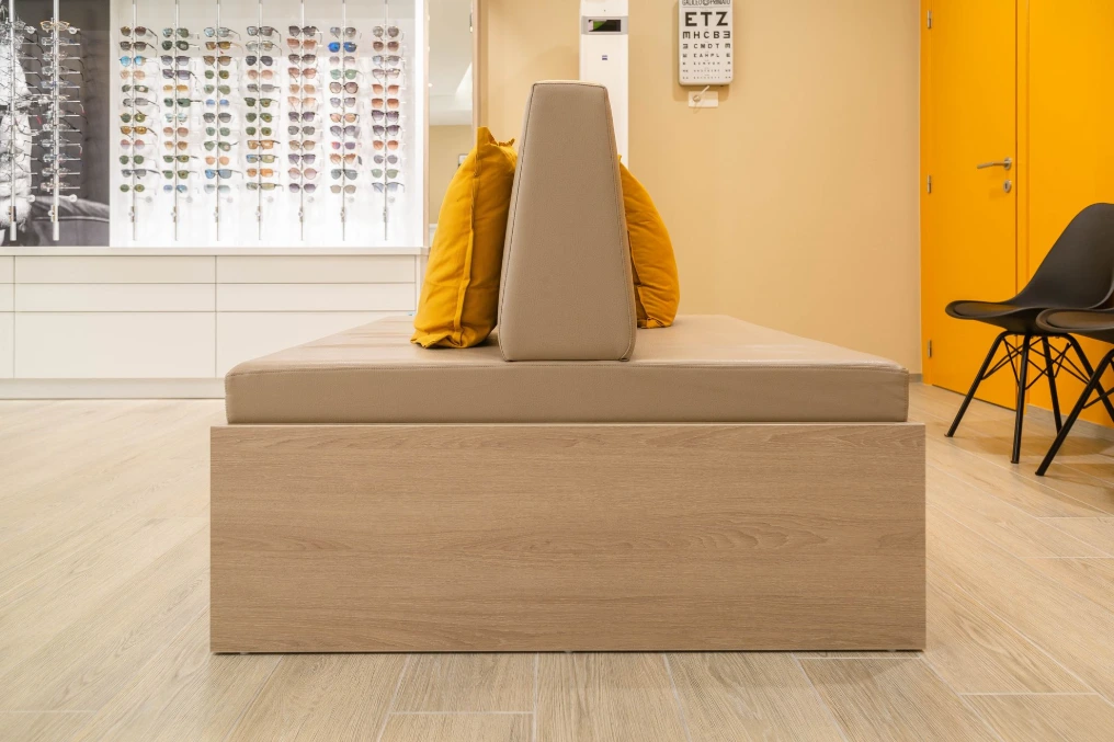 Coin attente : banquette en bois clair et mur de présentation — Optique Bernard