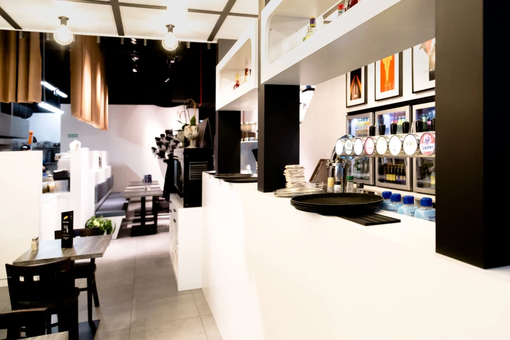 Espace de service : comptoir blanc, présentoirs et tables carrées — La Mise en Cène - Mons