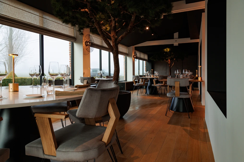 Salle avec baies vitrées, arbre intérieur et fauteuils gris — Le Bouchon et l'Assiette