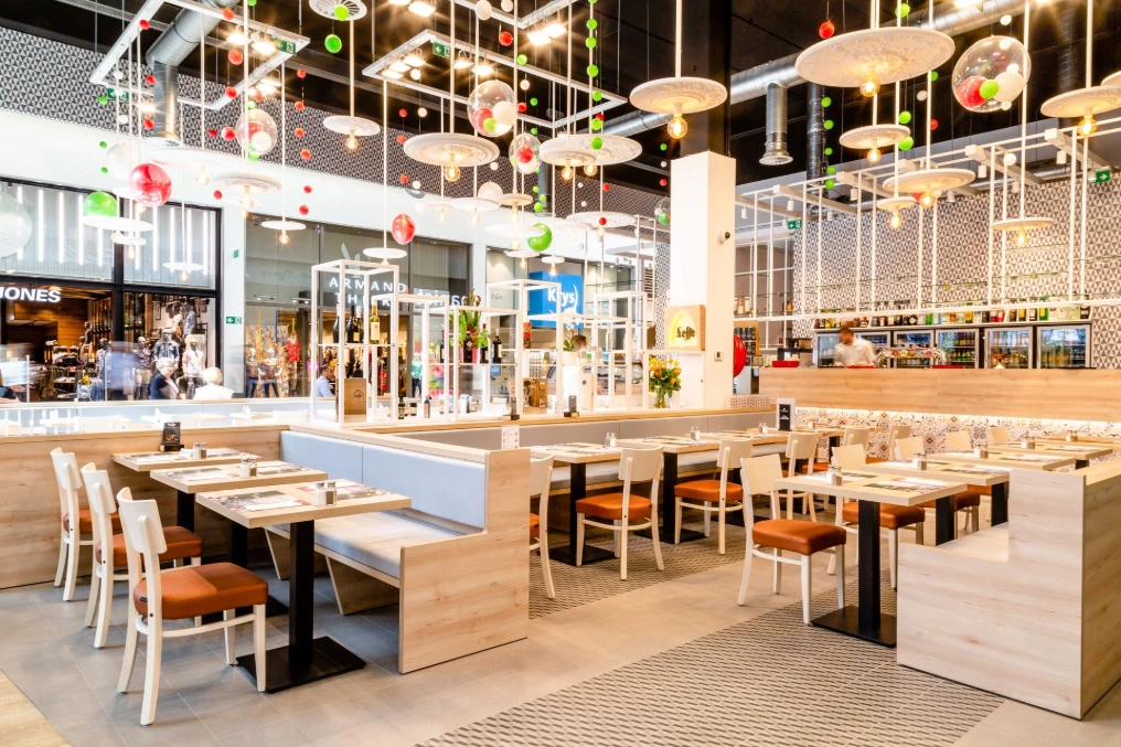 Salle : banquettes en cuir camel, tables claires et structure suspendue — La Vita e Bella - Bastions