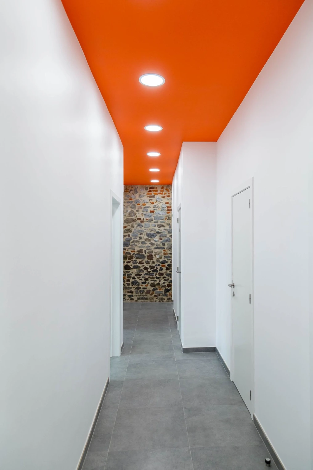 Couloir avec plafond orange et mur en pierre au fond — Centre vétérinaire Optimavet