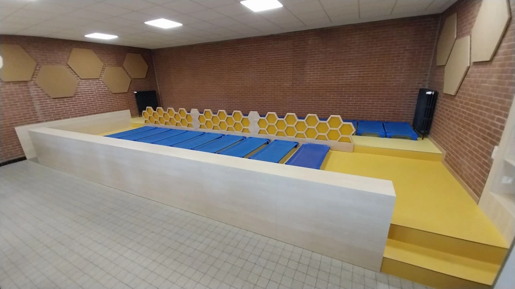 Salle avec estrade et tapis de sieste bleus et jaunes — École maternelle Morlanwelz