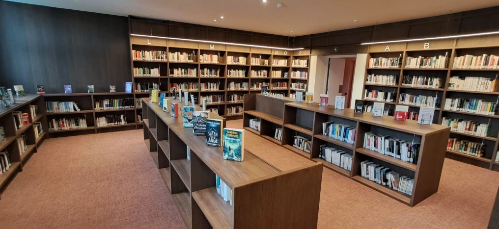 Rayonnages en bois sombre et banque de prêt — Bibliothèque Rebecq