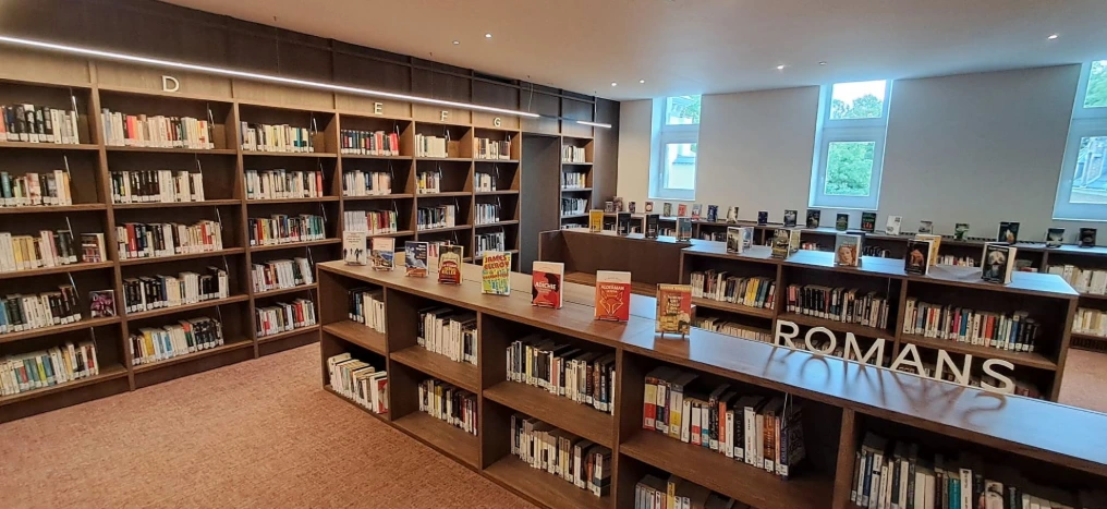 Longs rayonnages en bois clair et signalétique Romans — Bibliothèque Rebecq