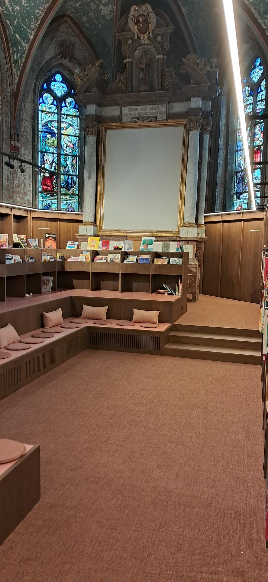 Espace lecture aménagé dans le chœur, sous les vitraux — Bibliothèque Rebecq
