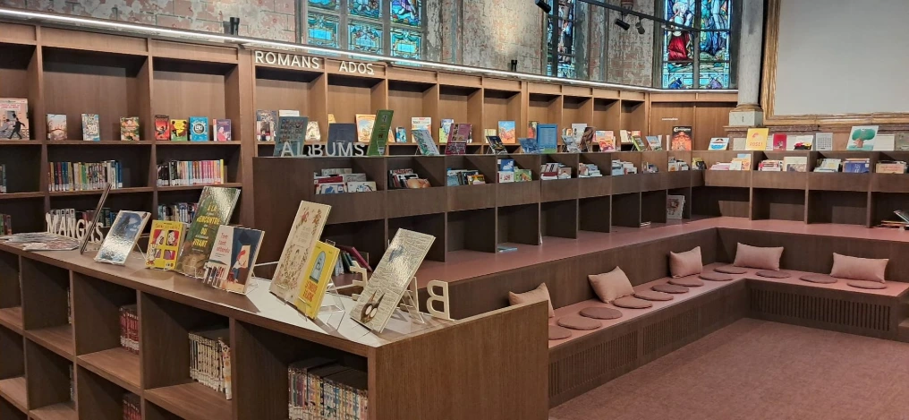 Rayonnages et présentoirs sous les vitraux de l'ancienne église — Bibliothèque Rebecq