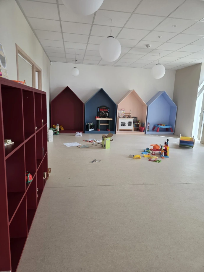 Salle de jeux avec meuble-bibliothèque bordeaux et maisonnettes murales — Crèche « Les bulles d'O »